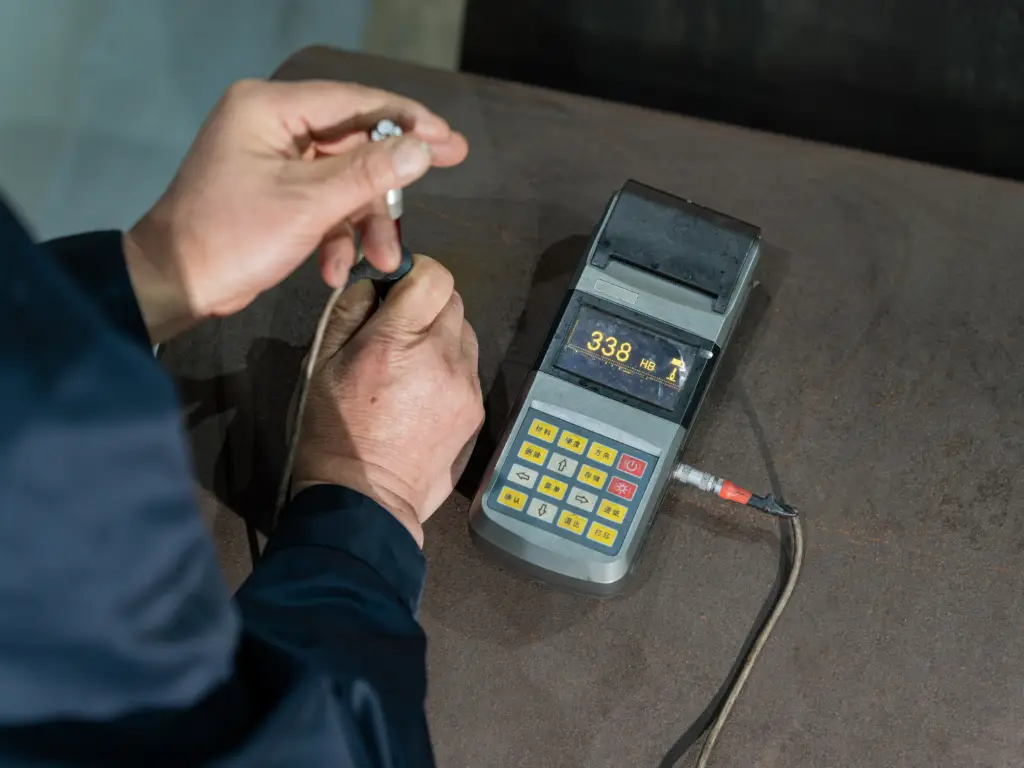 Close-up of a handheld hardness tester displaying a reading of '338 HB' on a metal surface.