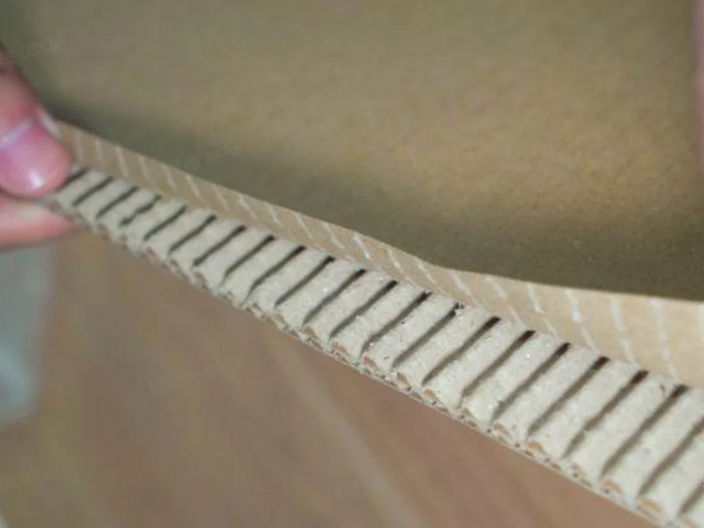 Technician peeling back the edge of corrugated board to show poor bonding between the inner liner and flutes. The visible white glue lines indicate a failure in the adhesive setting process, a core challenge for single facers