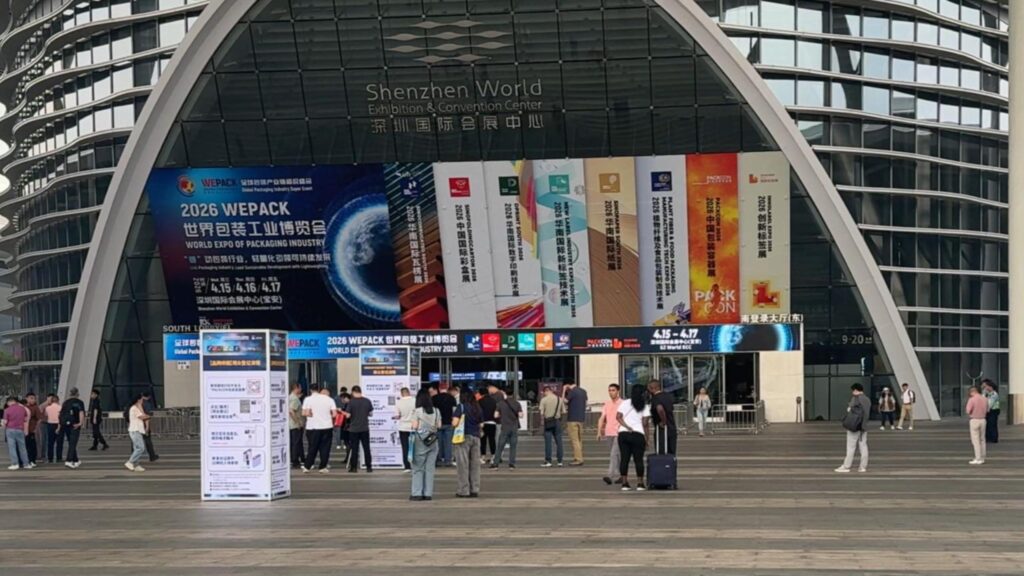 Shenzhen World Exhibition & Convention Center building facade showing advertisements for the 2026 WEPACK packaging expo and co-located trade shows, with attendees walking in front of the venue.