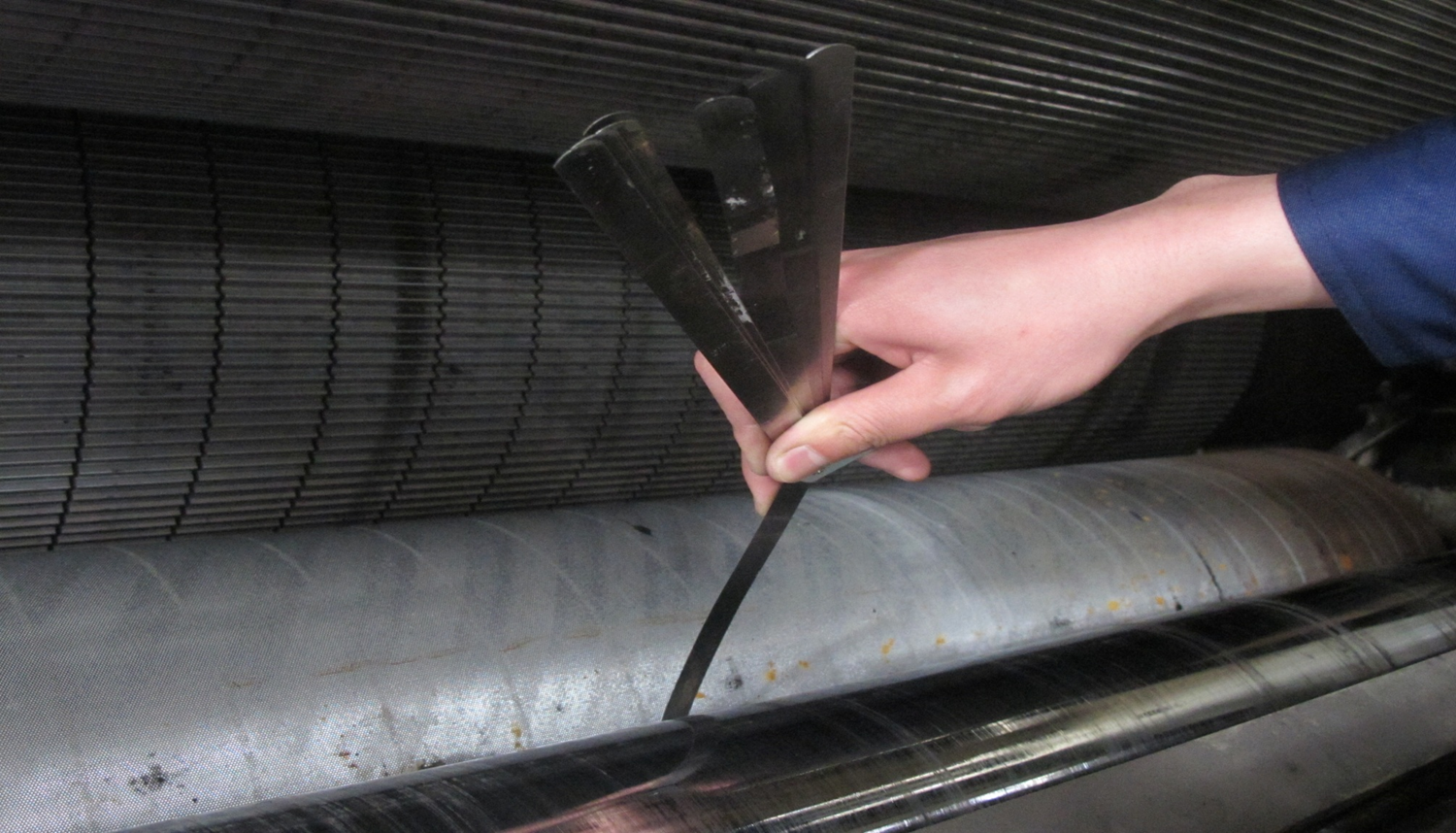 A technician using a feeler gauge on a corrugating roll